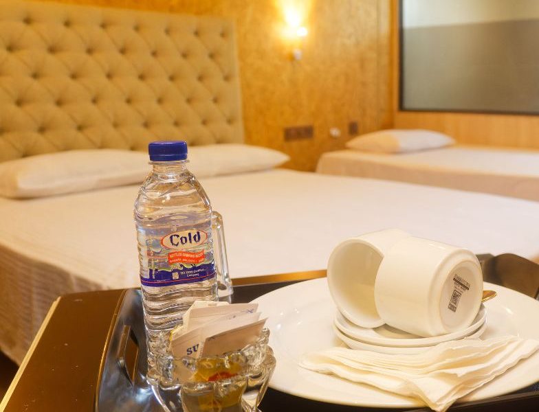 A neatly arranged bed in a budget-friendly triple room at Mon Ami City Hotel, showcasing a tray with water and coffee.