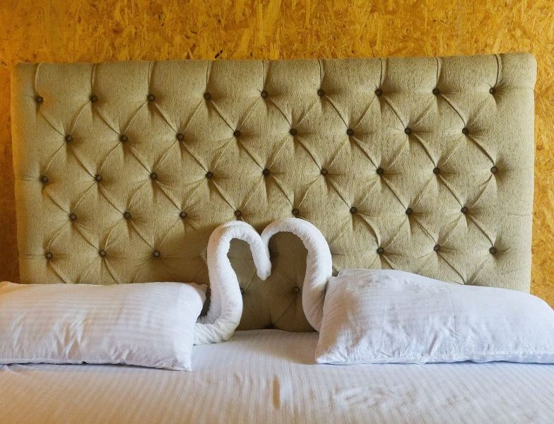 A neatly arranged bed featuring two elegant swan pillows, reflecting the clean and affordable accommodations at Mon Ami City Hotel.