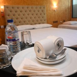 Inside a Mon Ami City Hotel double room, a bed adorned with two folded white towels and a cup placed atop the linens.