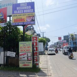 A street view showcasing a sign for a glass house, with the modern facade of Mon Ami City Hotel in the background.