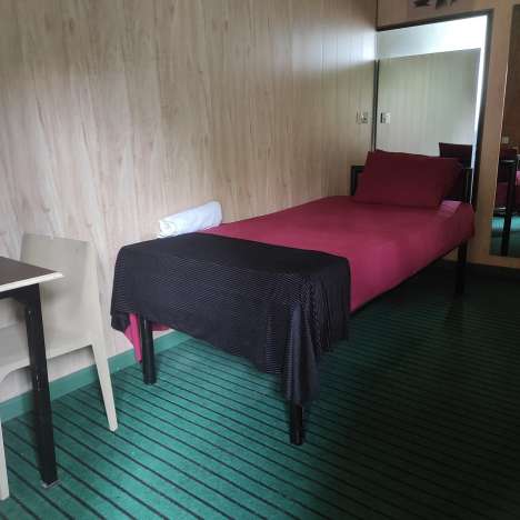 Interior of a Mon Ami City Hotel single room showcasing a bed, a mirror, and a chair, designed for comfort and relaxation.